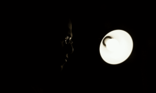 פנים של אדם המביט בחושך וברקע שלו מאירה מנורת לילה קטנה