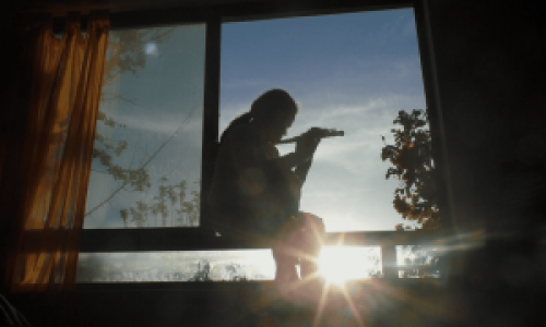 בחורה צעירה יושבת על חלון ומנגנת בחליל צד